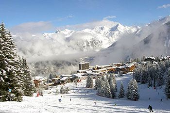 Snow-covered Courchevel village and a ski slope with skiers against the mountains